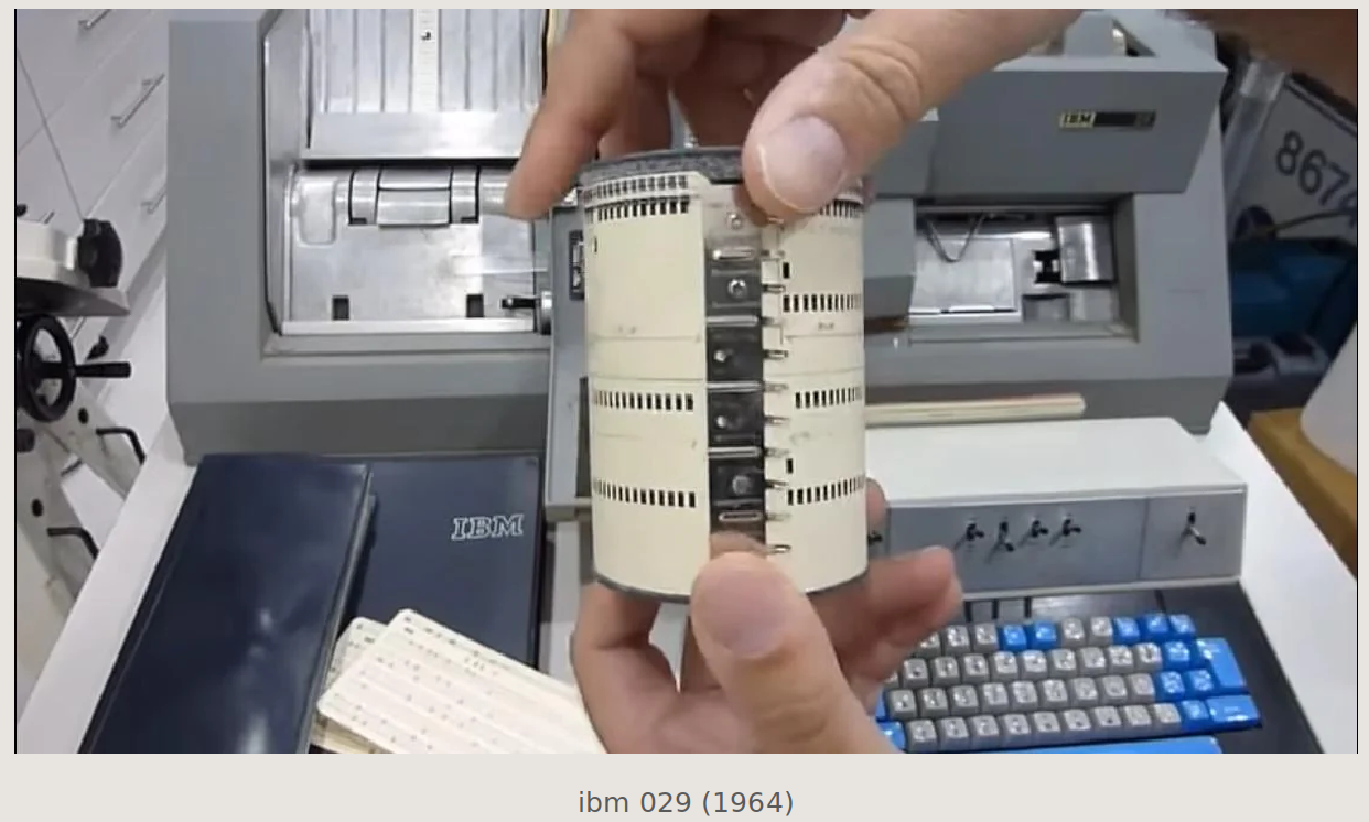 A person's hands holding a thick stack of punched cards over an IBM 029 card punch machine from 1964, with its blue keyboard and card hopper visible. Caption in the image reads: ibm 029 (1964).